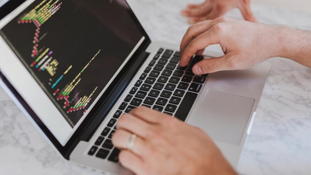 Handen typen HTML-code op een laptop, illustratie bij text salting in phishingmails die AI-spamfilters omzeilt