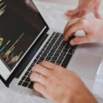 Handen typen HTML-code op een laptop, illustratie bij text salting in phishingmails die AI-spamfilters omzeilt