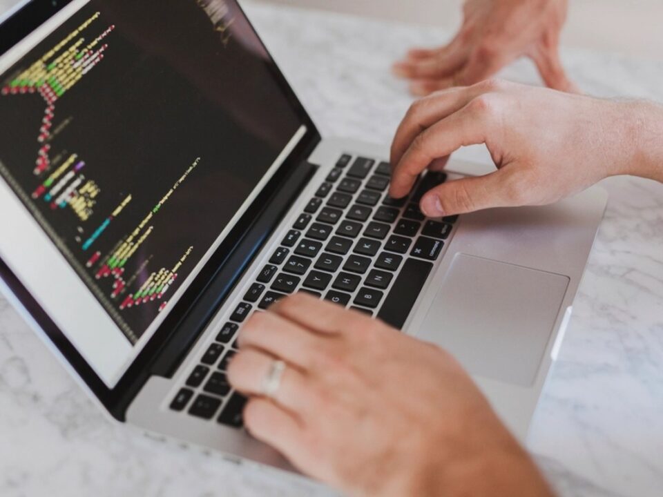 Handen typen HTML-code op een laptop, illustratie bij text salting in phishingmails die AI-spamfilters omzeilt